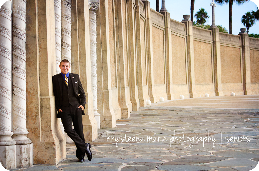 senior portrait guy in suit leaning against wall at lake