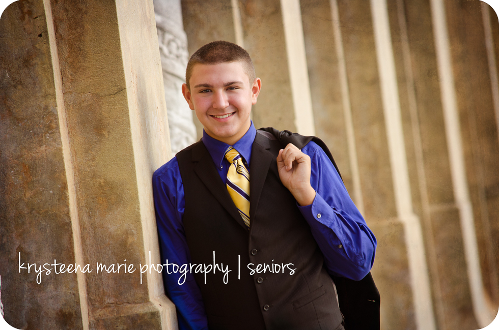 high school senior boy in suit leaning against wall, jacket over shoulder