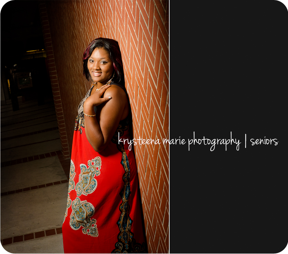 high school senior girl resting on brick wall red dress