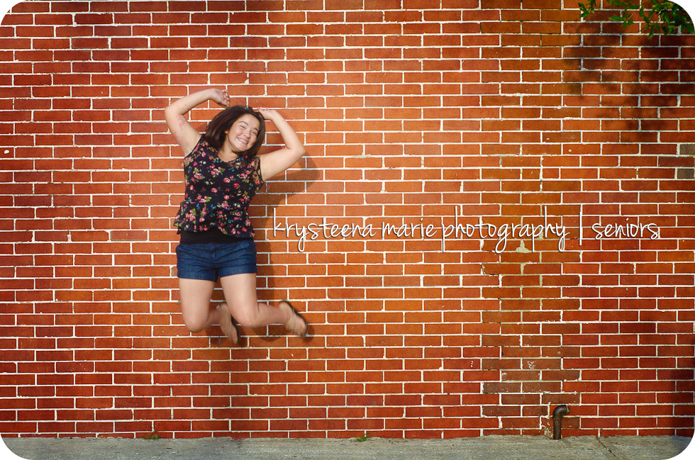 Senior portrait Chelsea jumping for joy brick wall